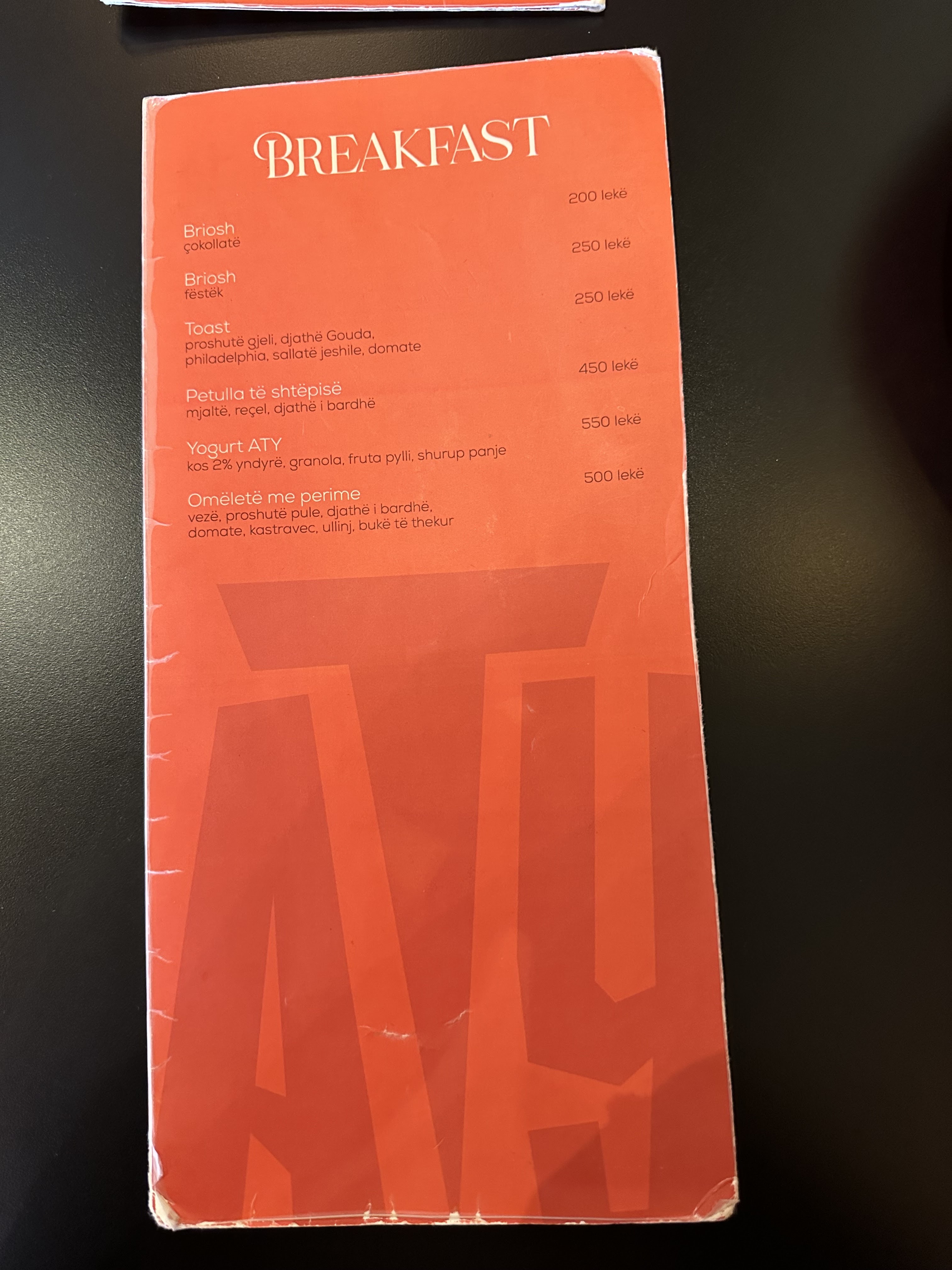 The printed ATY breakfast menu in signature coral-red with the oversized ATY monogram